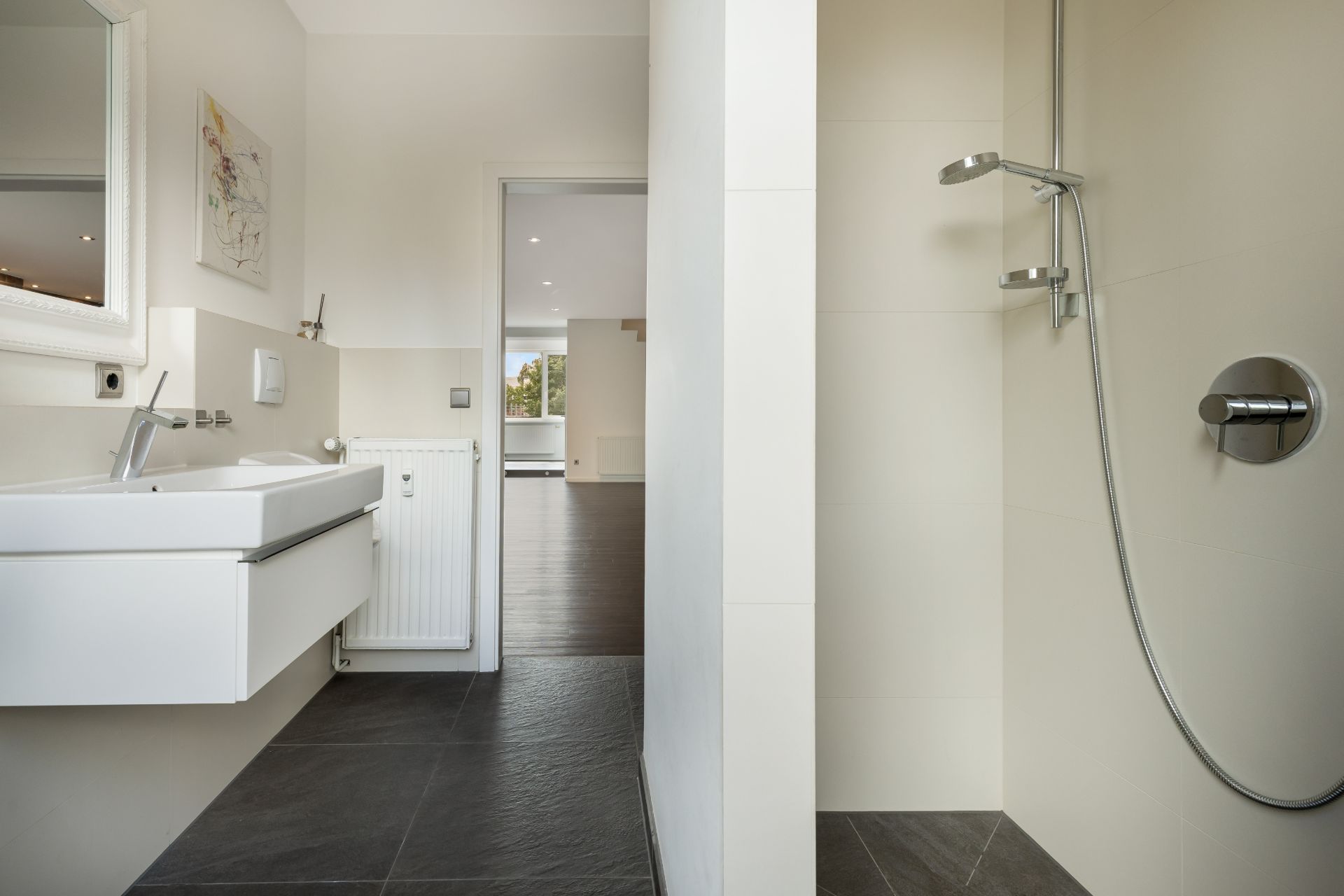 Modernes Badezimmer mit Waschbecken, Spiegel und offener Dusche, Blick in einen hellen Wohnbereich.
