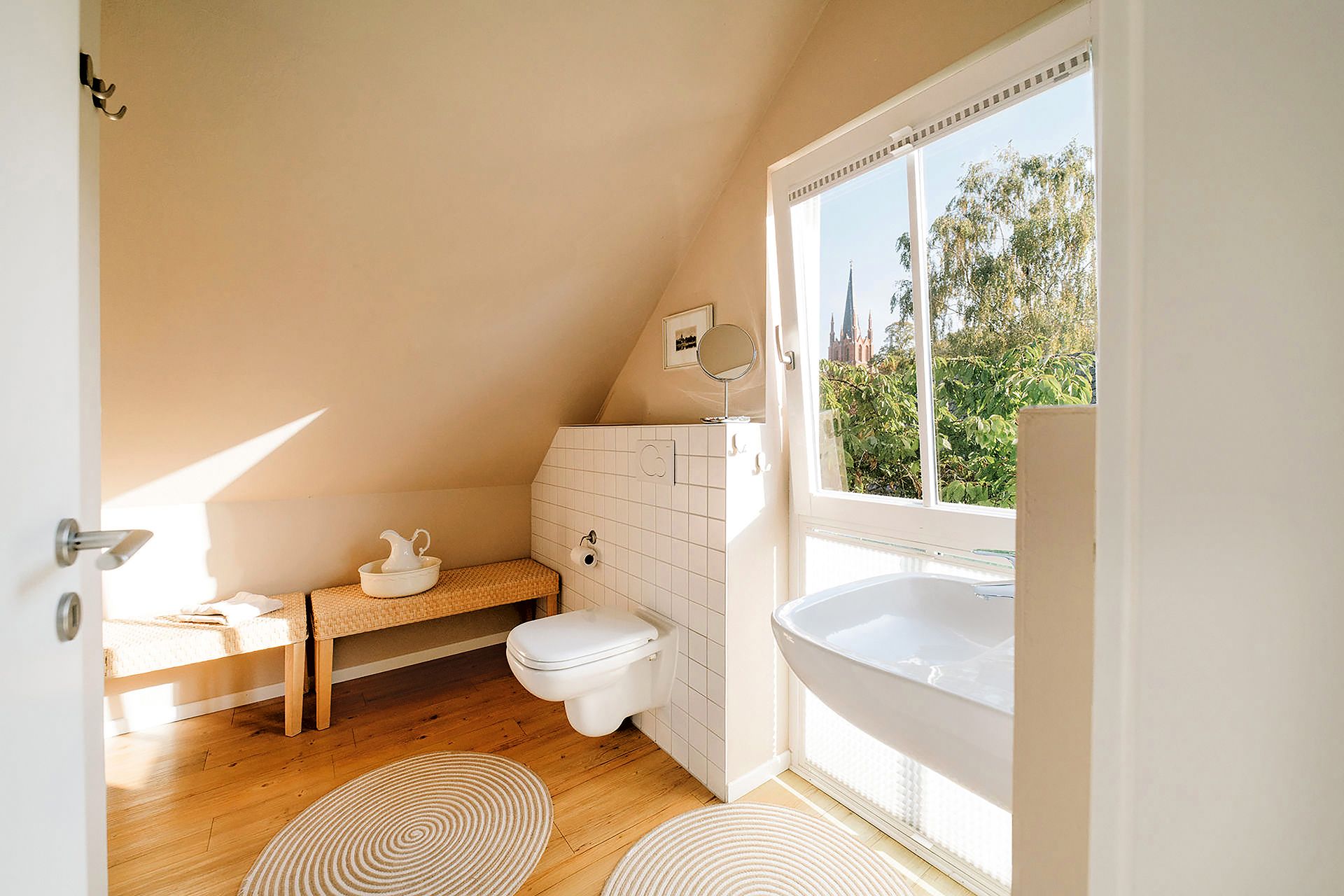 Helles Badezimmer mit schwebender Toilette, Waschbecken, Bank und großem Fenster mit Ausblick.