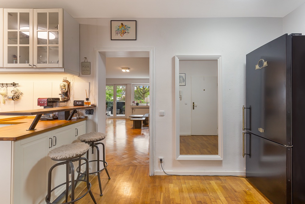 Moderne Küche mit Theke und zwei Hockern, Blick ins Wohnzimmer mit Holzfußboden.