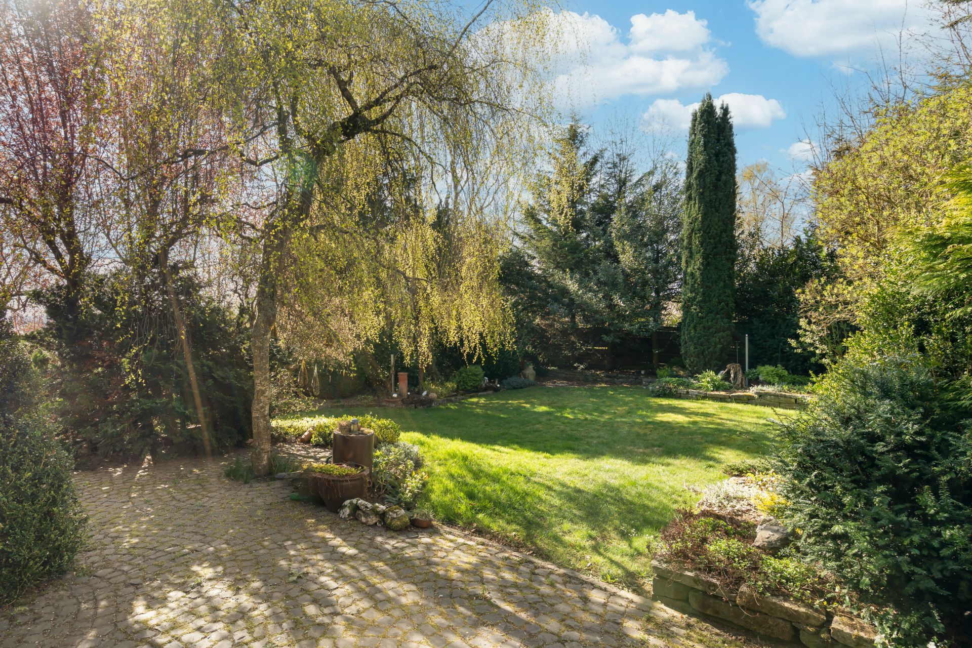 Grüner Garten mit Rasen, Bäumen und gepflastertem Weg an einem sonnigen Tag.