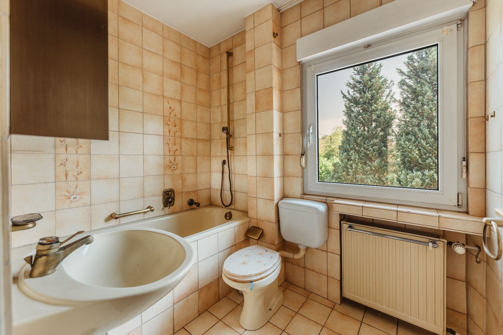 Badezimmer mit Badewanne, Waschbecken, Toilette und großem Fenster mit Blick auf Bäume.