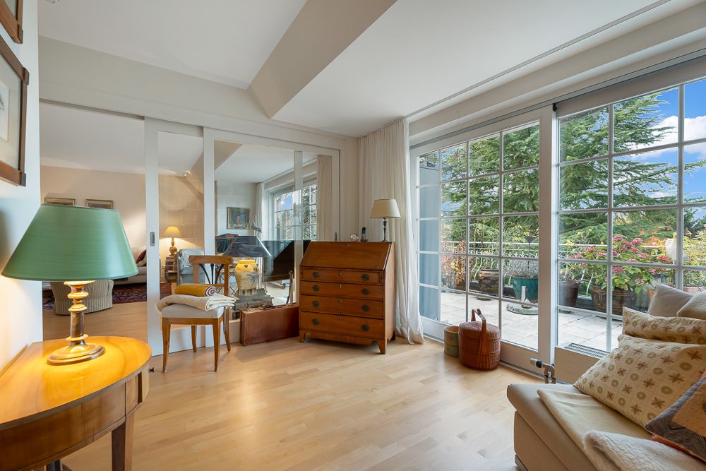 Helles Wohnzimmer mit großen Fenstern, Holzboden, Sofa und Zugang zur Terrasse mit Pflanzen.