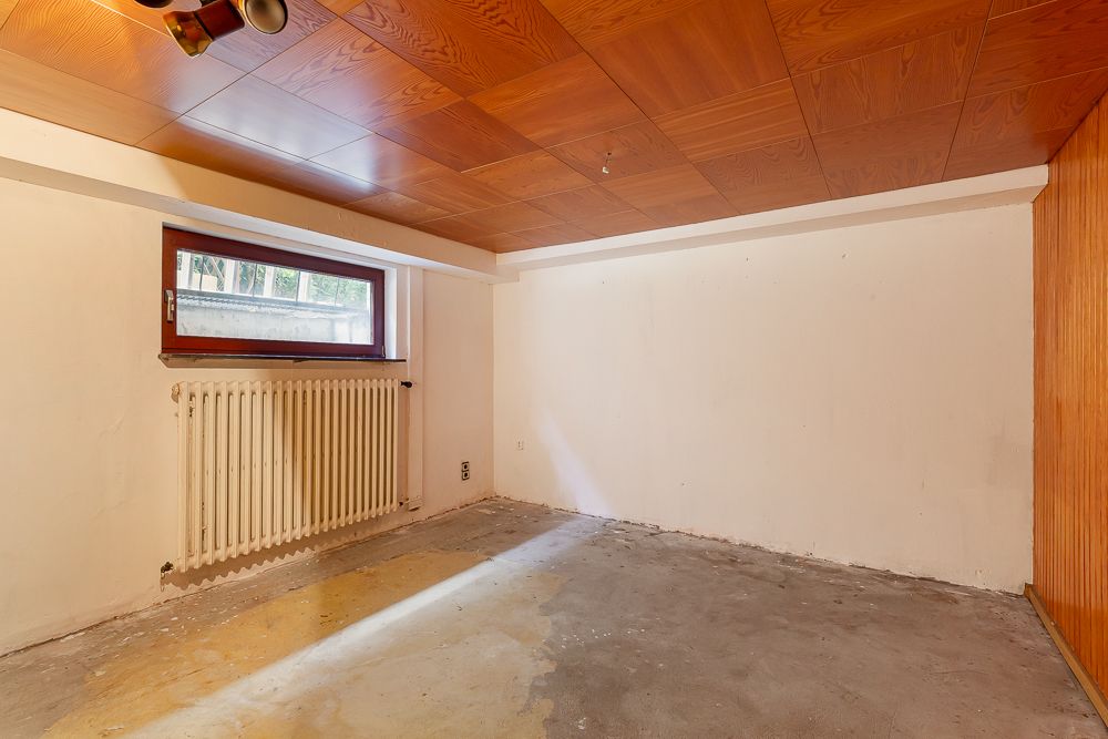 Leerer Raum mit Holzbalkendecke, kleinem Fenster, Heizkörper und kahlem Boden.
