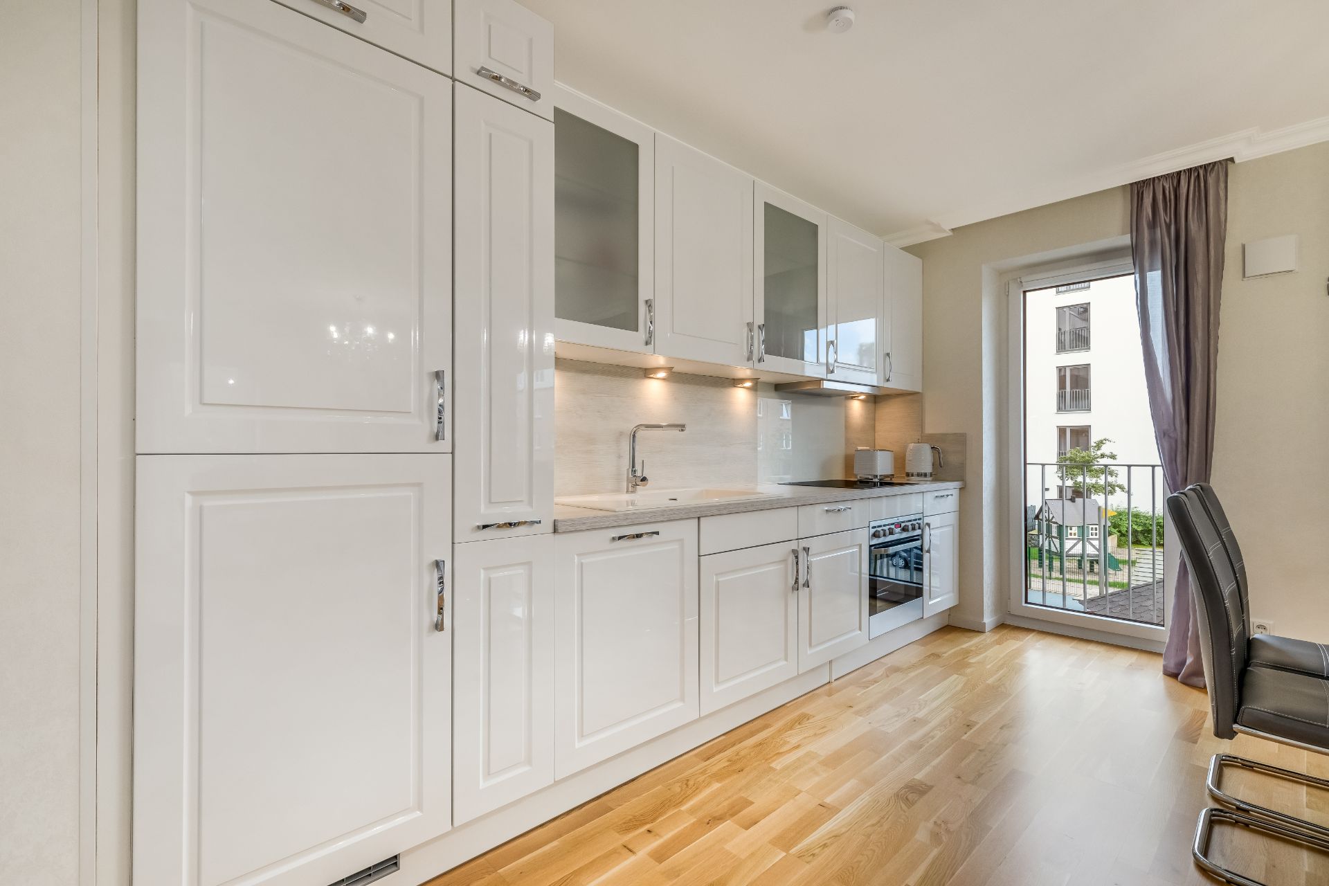 Moderne weiße Einbauküche mit Holzboden und großem Fenster mit Blick nach draußen.