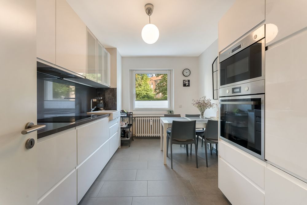 Moderne Küche mit weißen Schränken, Esstisch, vier Stühlen und Fenster mit Blick ins Grüne.