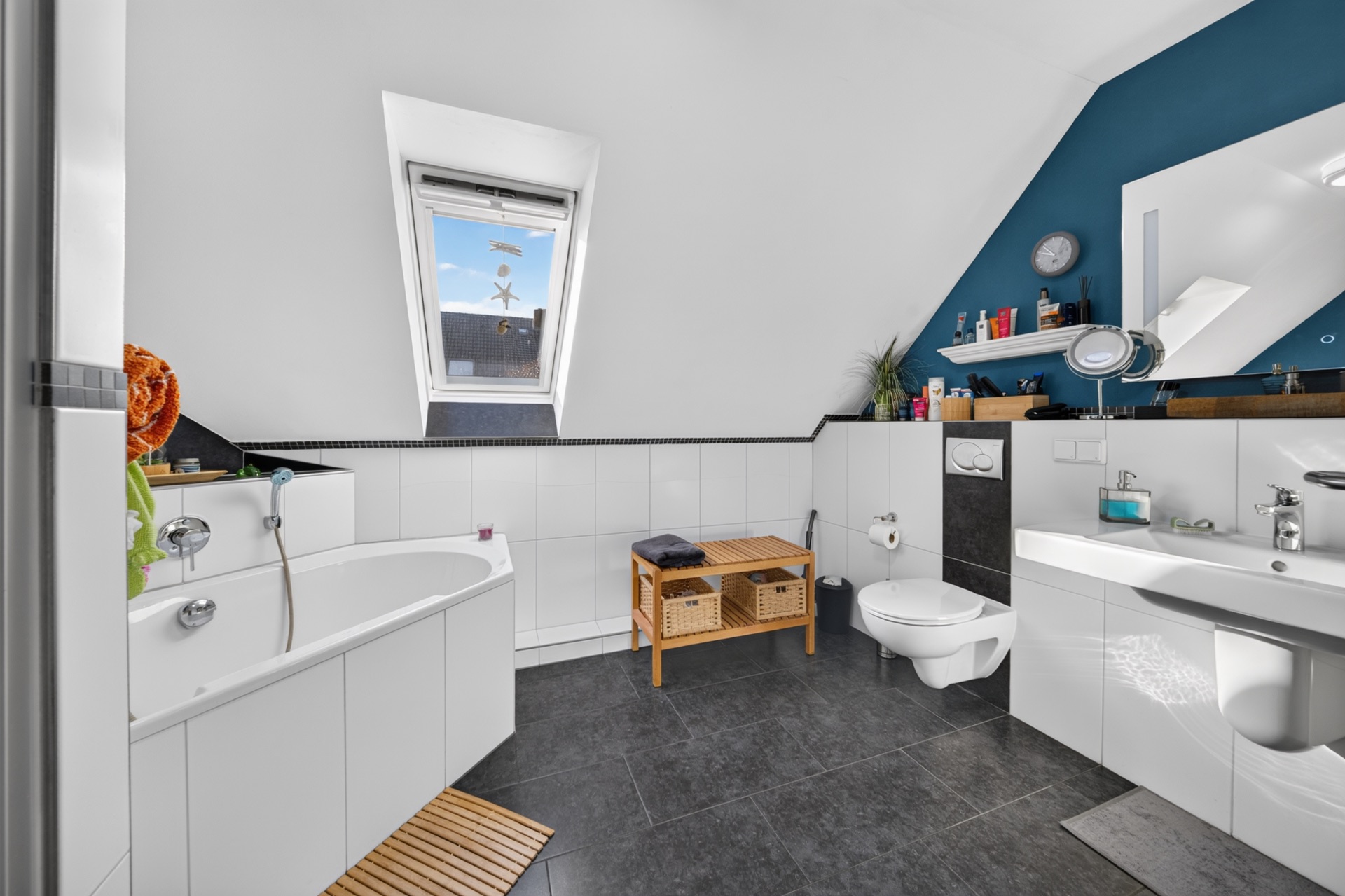 Modernes Badezimmer mit Badewanne, Waschbecken, WC, Holzbank und Dachfenster.