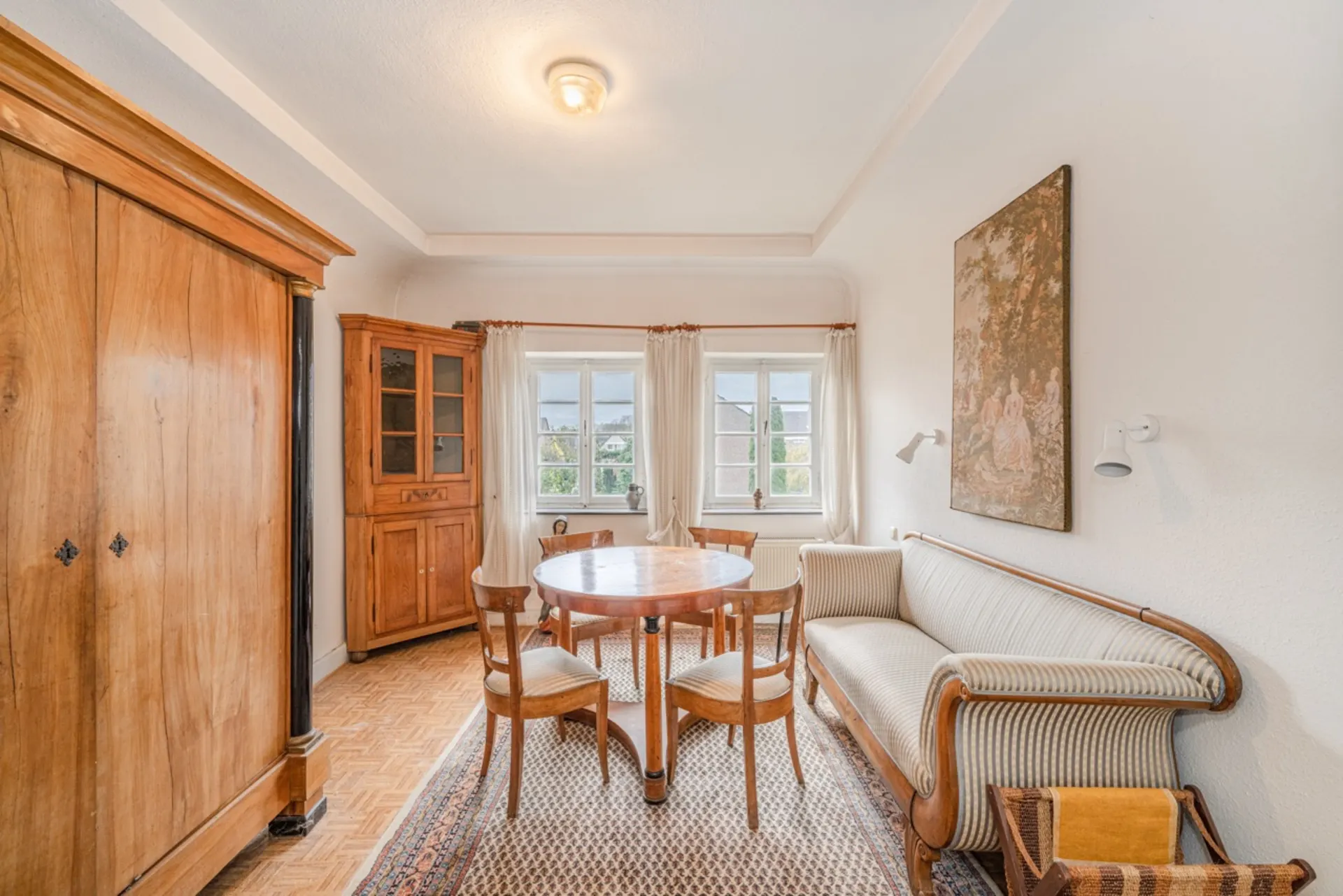 Heller Wohnraum mit Holzmöbeln, rundem Tisch, Sofa und großen Fenstern.