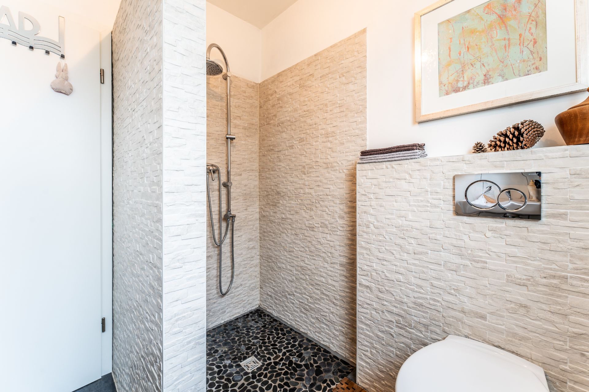 Modernes Badezimmer mit offener Dusche, Steinfliesen und Dekoration auf der Ablage.