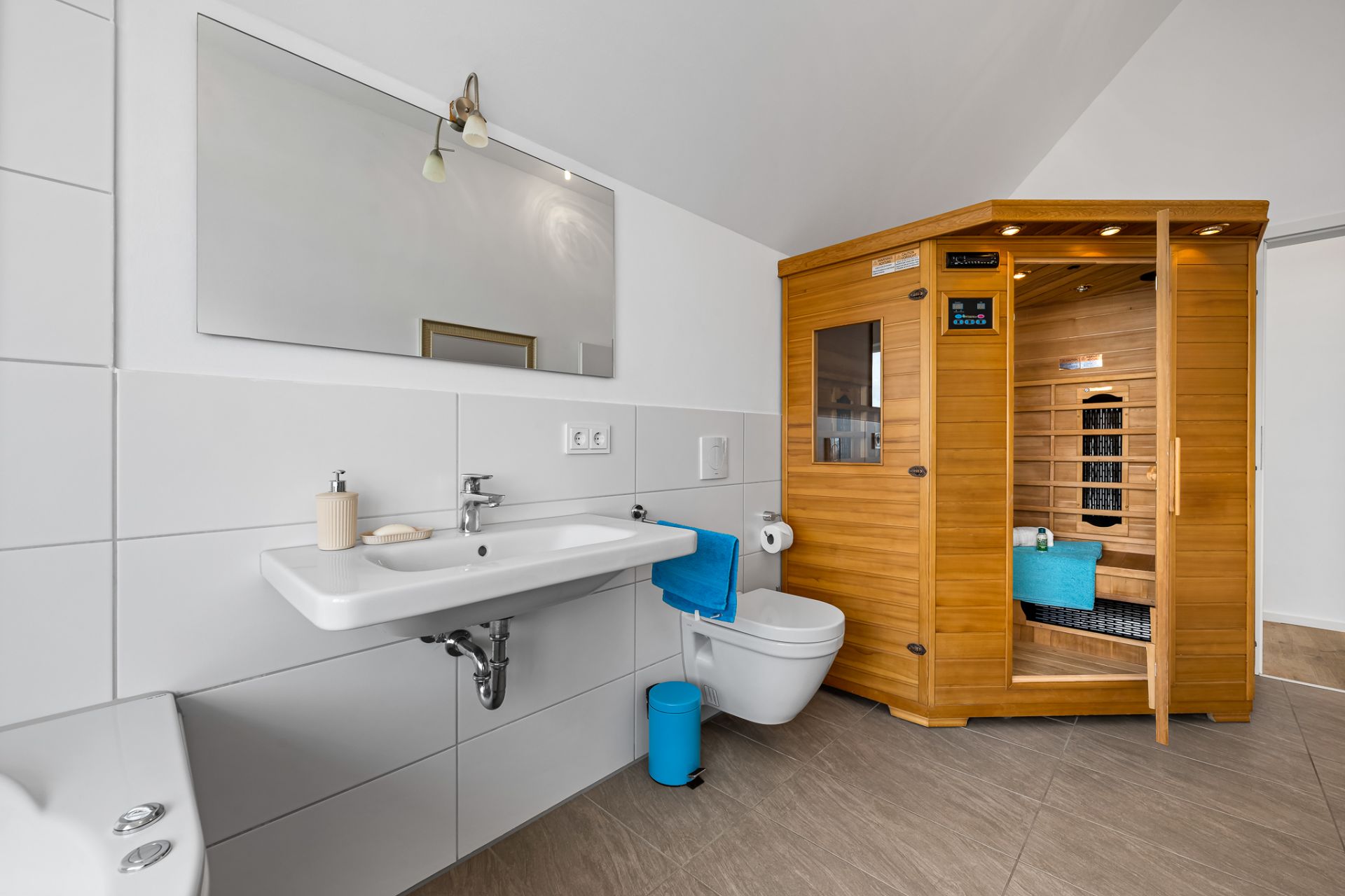 Modernes Badezimmer mit Waschbecken, Wandtoilette und Holzsauna.