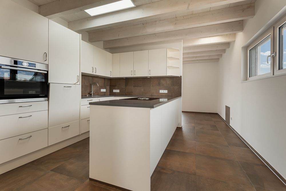Moderne Küche mit weißen Schränken, Kücheninsel und braunen Fliesenboden.