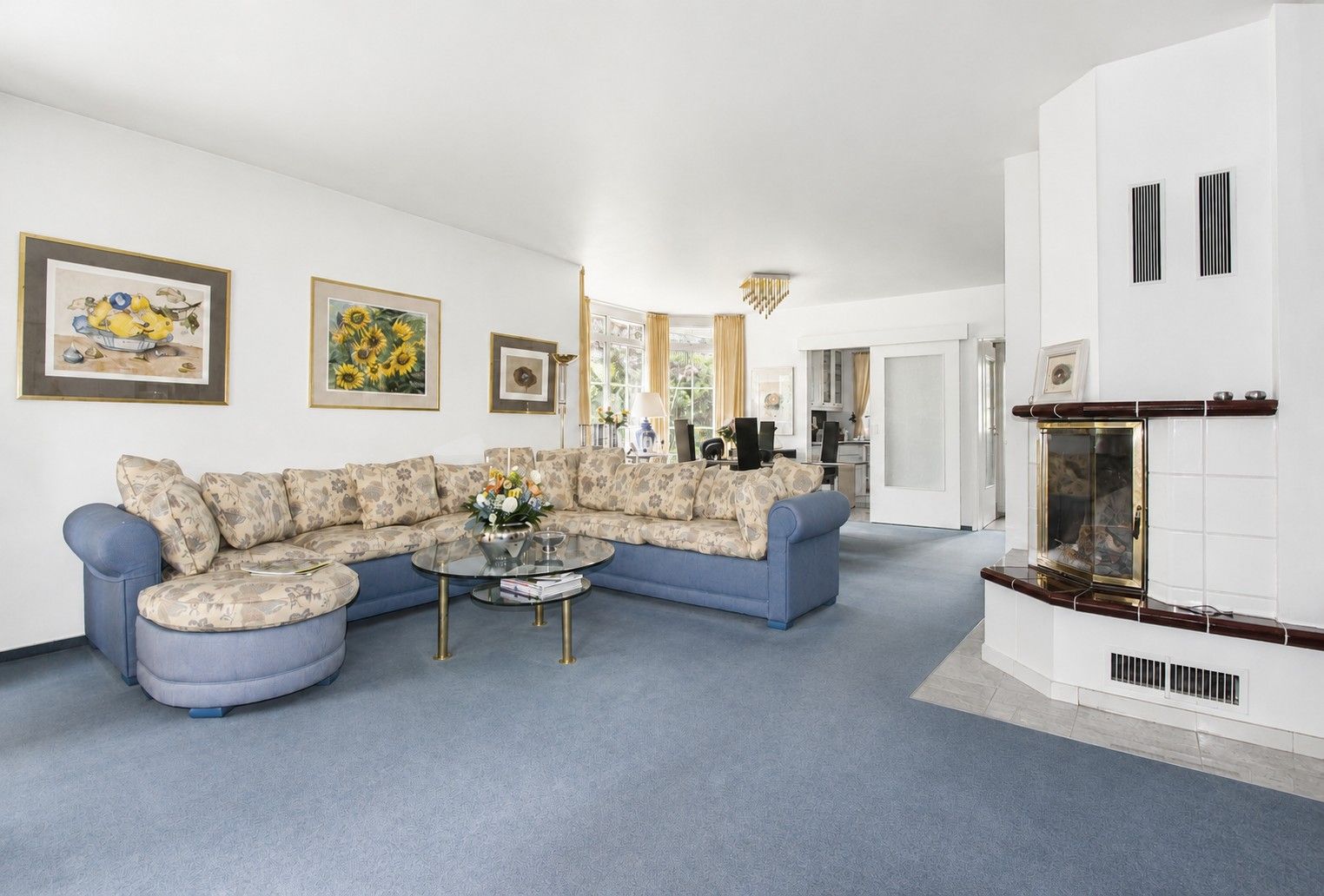 Wohnzimmer mit großer Eckcouch, Glastisch, Kamin und Bildern an der Wand.