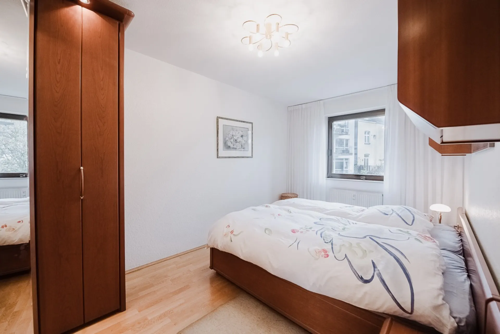 Helles Schlafzimmer mit Doppelbett, Holzschränken, Fenster und heller Deckenleuchte.