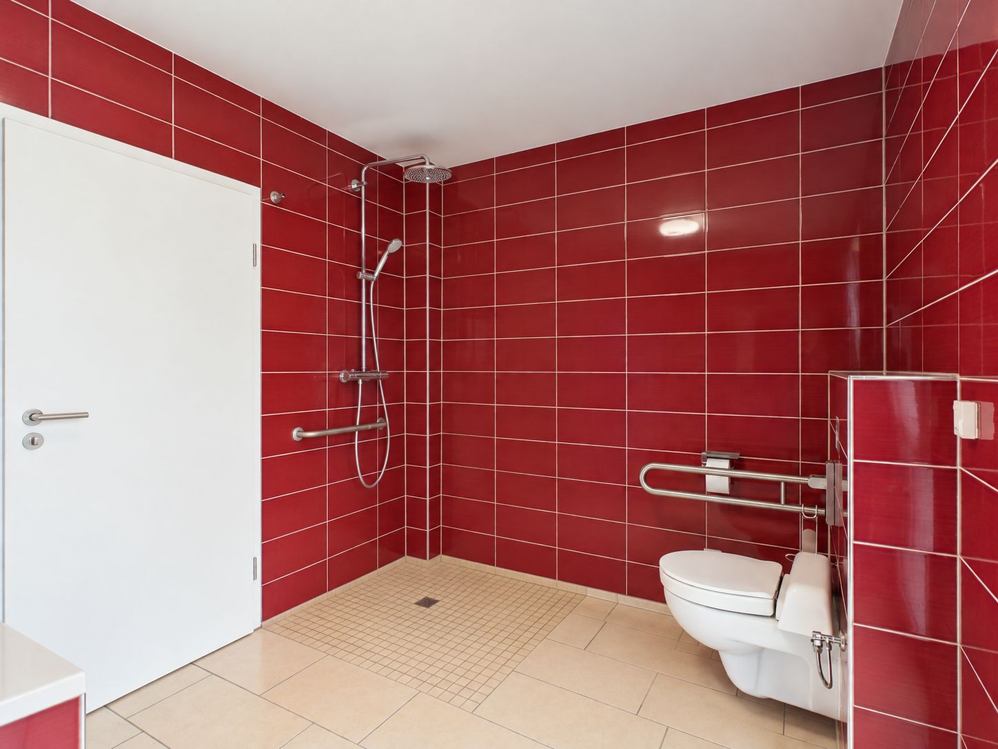 Badezimmer mit roten Fliesen, offener Dusche und Wand-WC mit Haltegriffen.