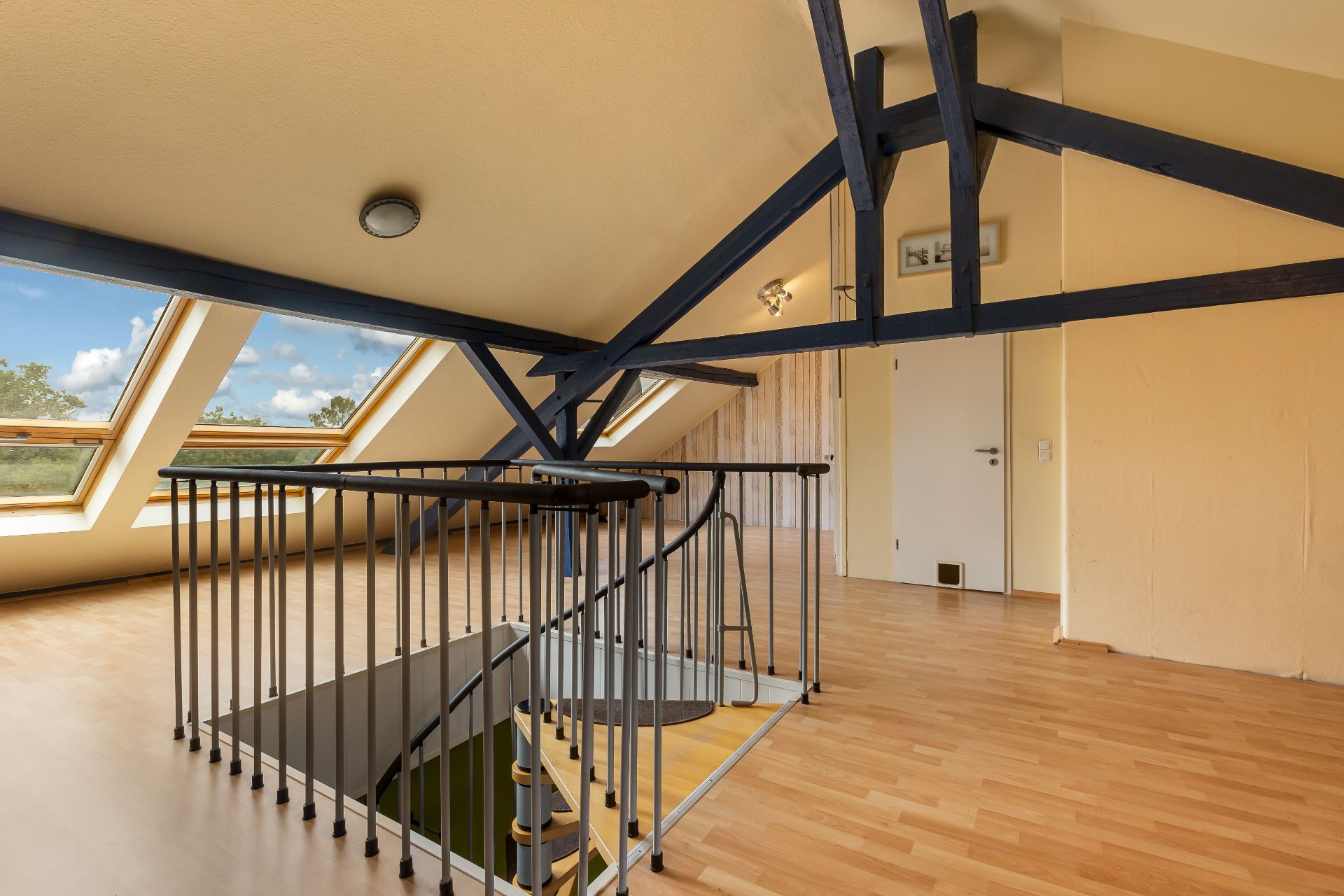 Helles Dachgeschoss mit Holztreppe, Dachfenstern und sichtbaren Balken.