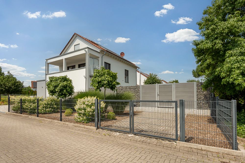 Modernes Einfamilienhaus mit Garten, Zaun und Einfahrt an einer ruhigen Straße.