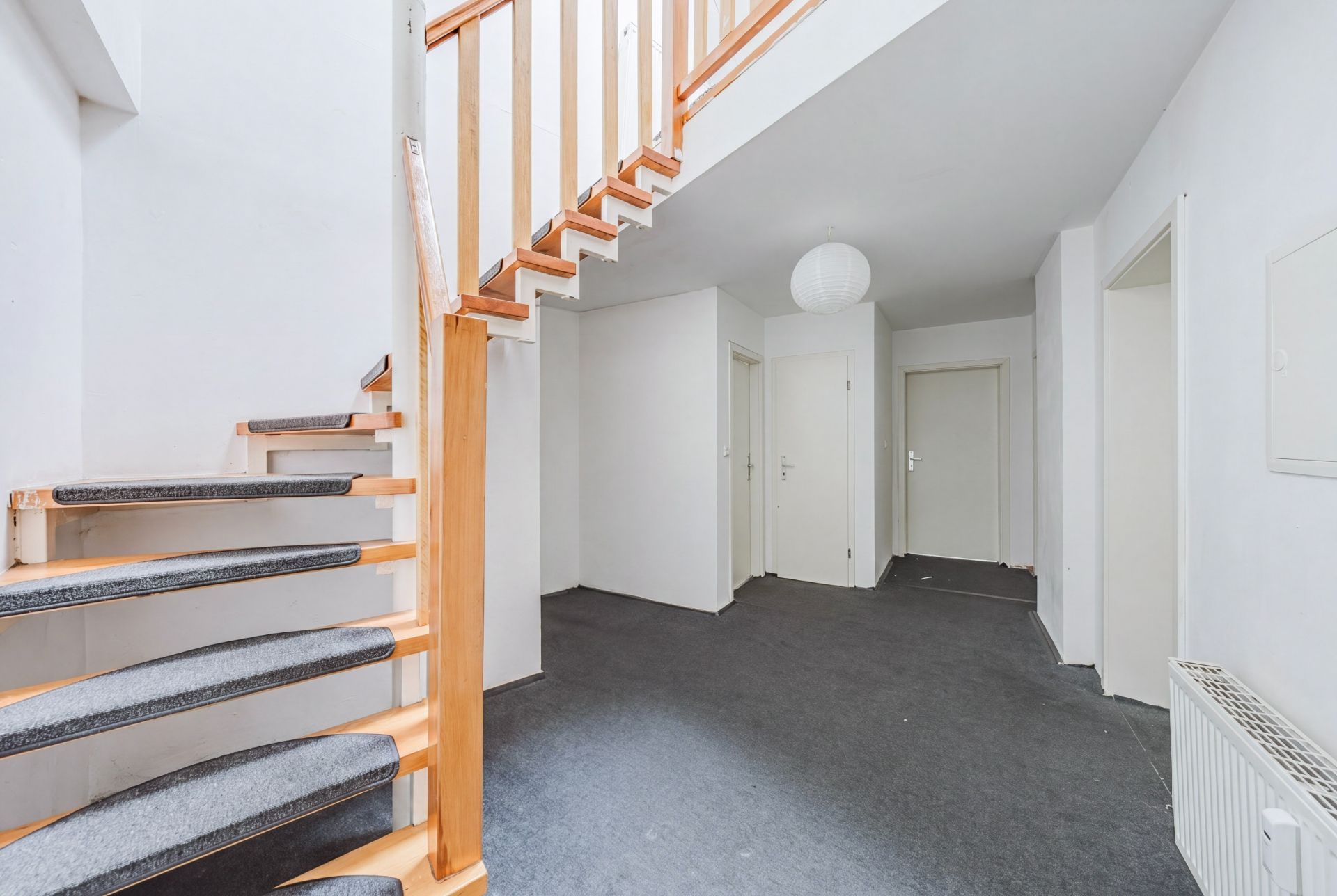 Heller Flur mit Teppichboden, Holztreppe und mehreren Türen zu angrenzenden Räumen.