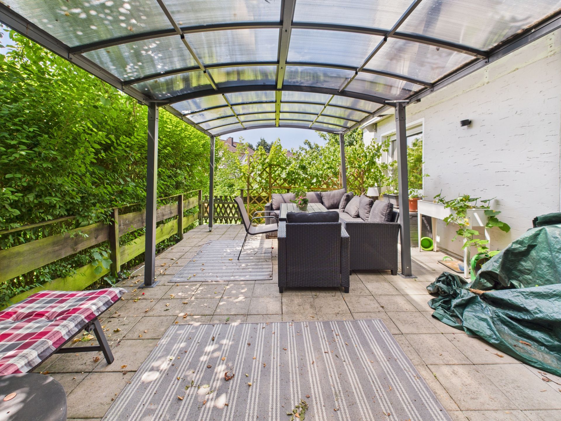 Überdachte Terrasse mit Sitzgruppe, Pflanzen und Blick ins Grüne.