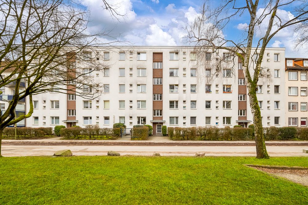 Mehrstöckiges Wohngebäude mit vielen Fenstern und Bäumen im Vordergrund.