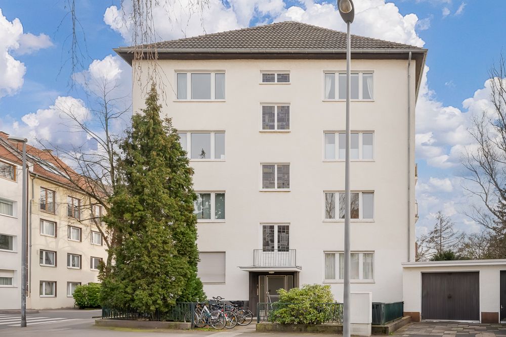 Vorderansicht eines vierstöckigen Wohngebäudes mit weißen Fenstern und einer Garage rechts.