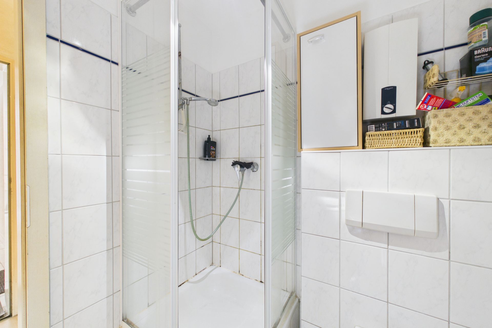 Gefliestes Badezimmer mit Duschkabine und Wandregal über der Toilette.