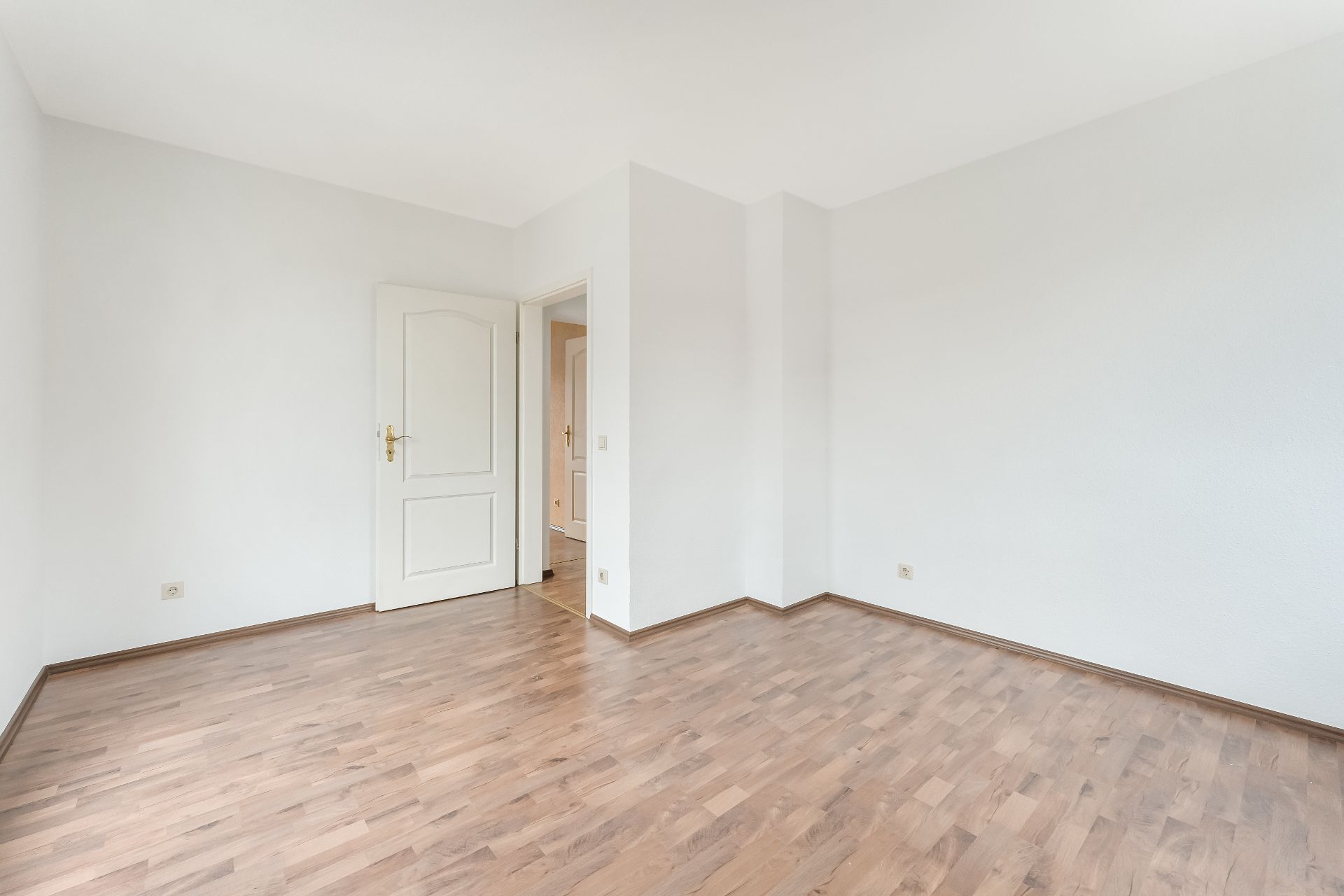 Leerer Raum mit Holzfußboden, weißen Wänden und geöffneter weißer Tür.