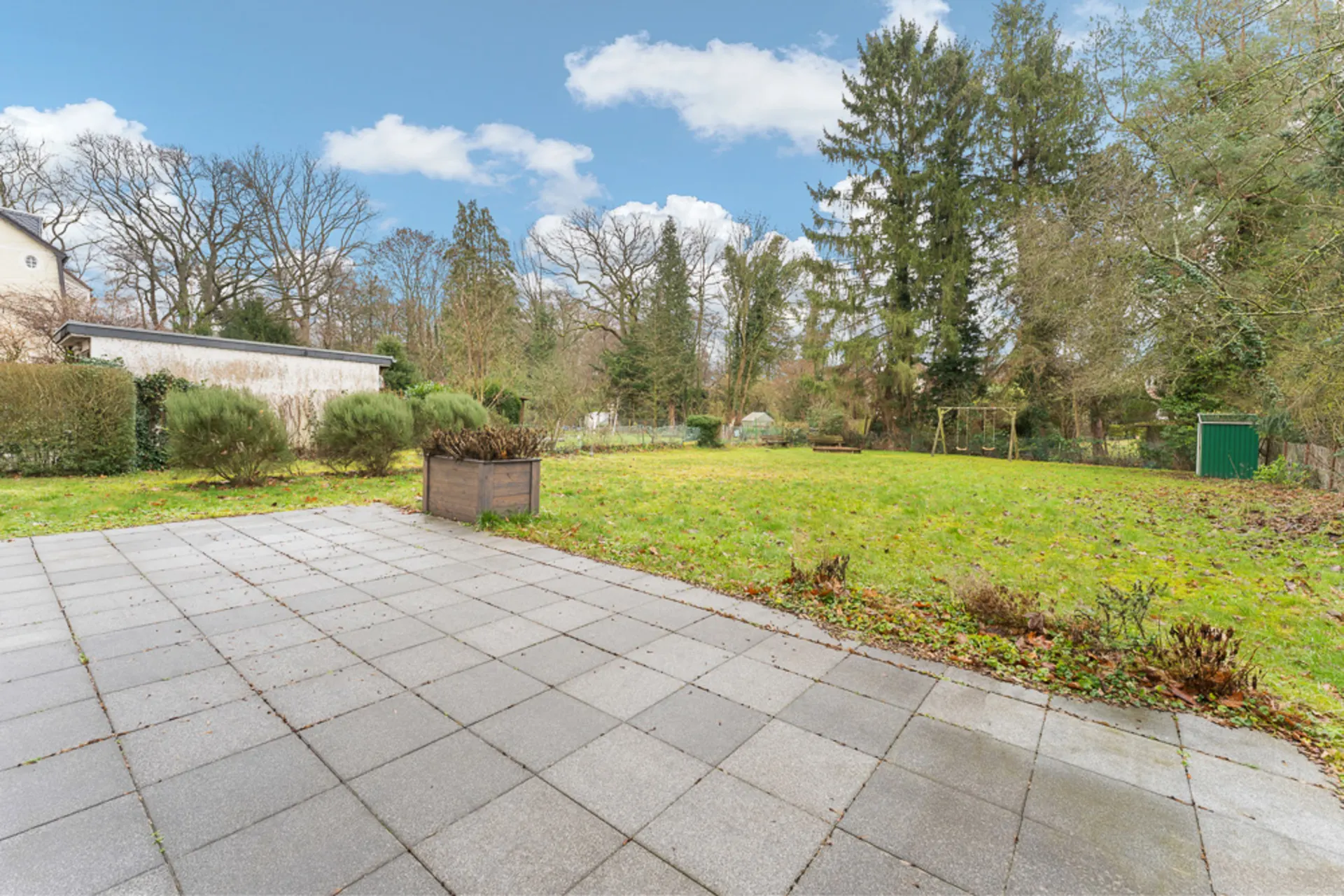 Gepflasterte Terrasse mit Blick auf einen großen Garten mit Rasen und Bäumen.