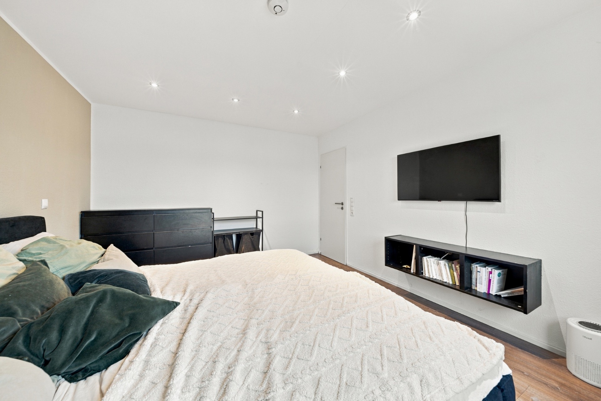 Schlafzimmer mit Bett, Fernseher an der Wand, Regal und Kommode mit Schreibtisch.