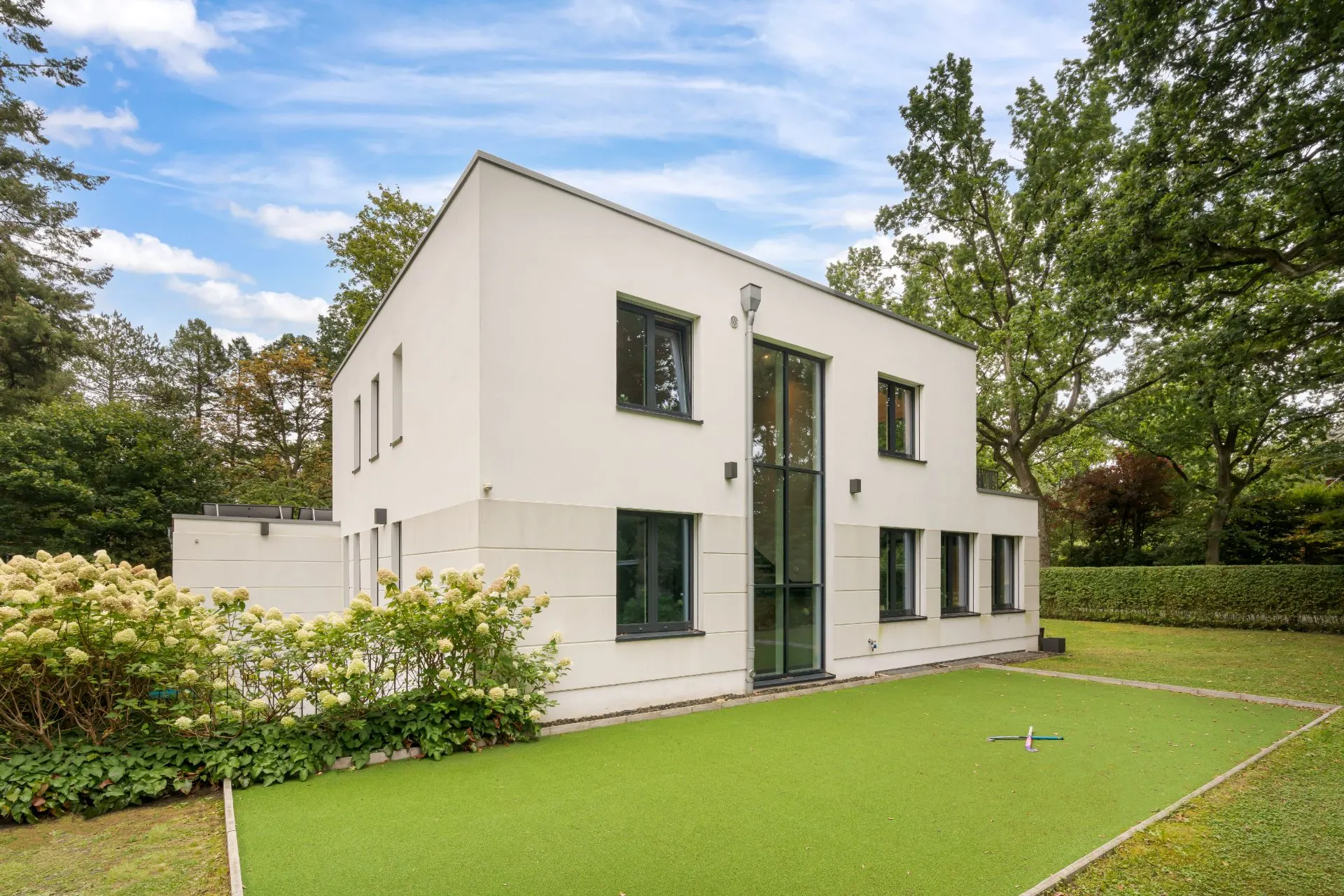 Modernes, weißes Wohnhaus mit Flachdach und großen Fenstern im Garten mit grünem Rasen.