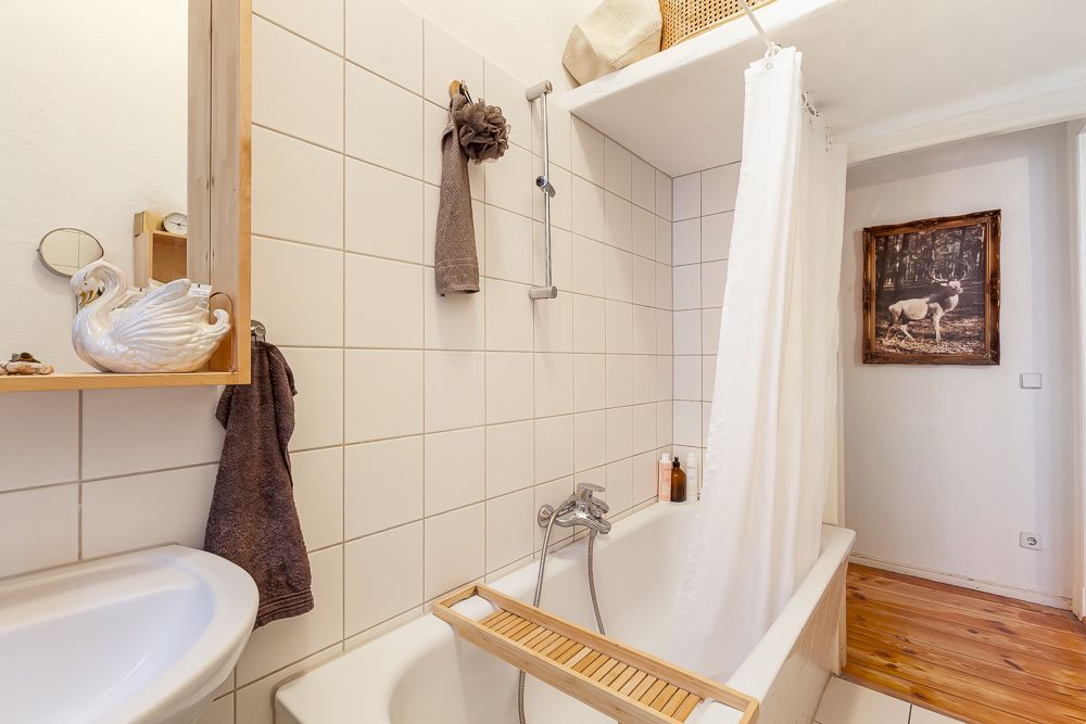 Helles Badezimmer mit Badewanne, Duschvorhang und Regal mit Schwanenfigur.