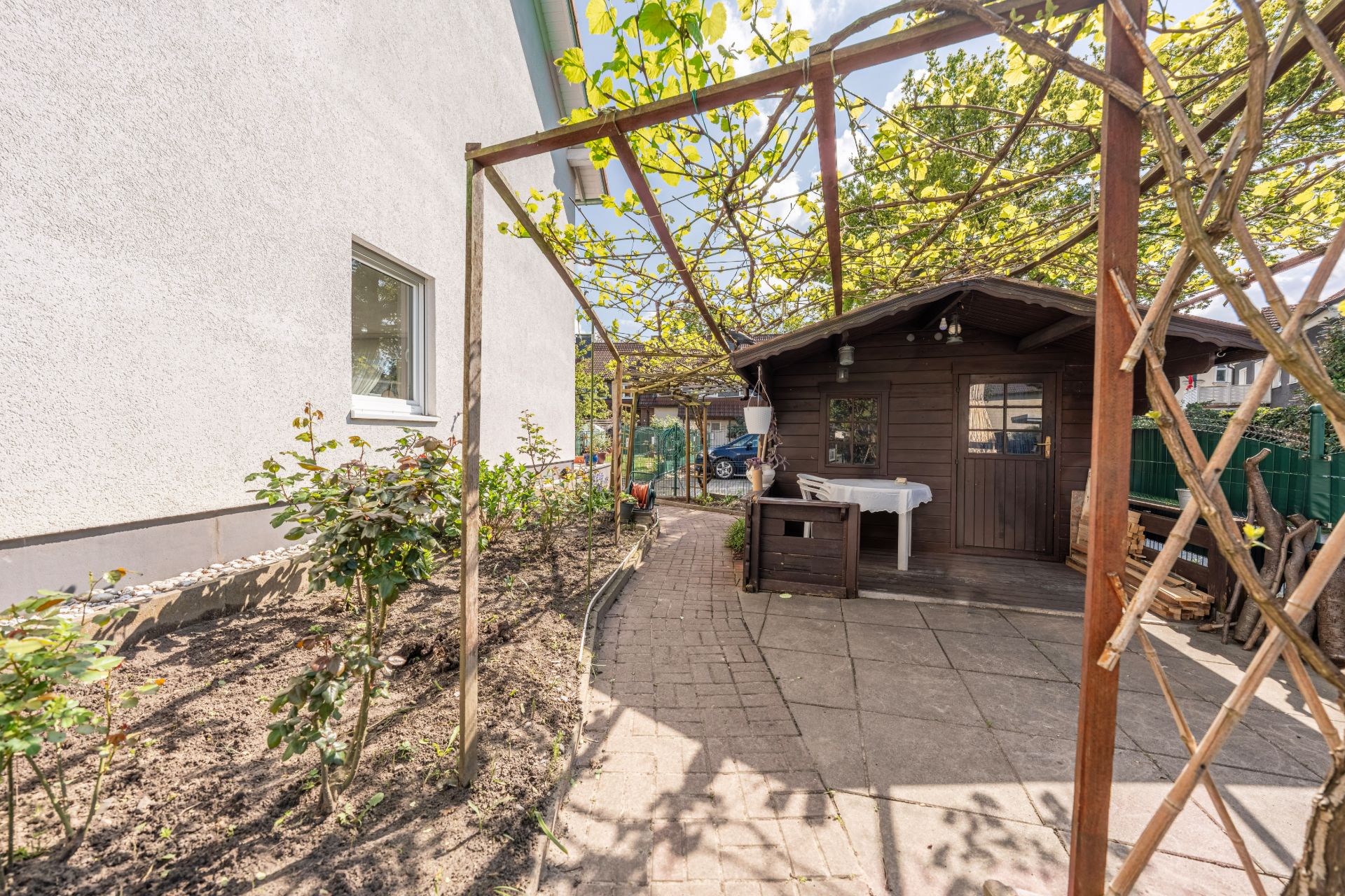 Garten mit kleinem Holzhaus, Pflasterweg und Pflanzen neben einem weißen Wohnhaus.