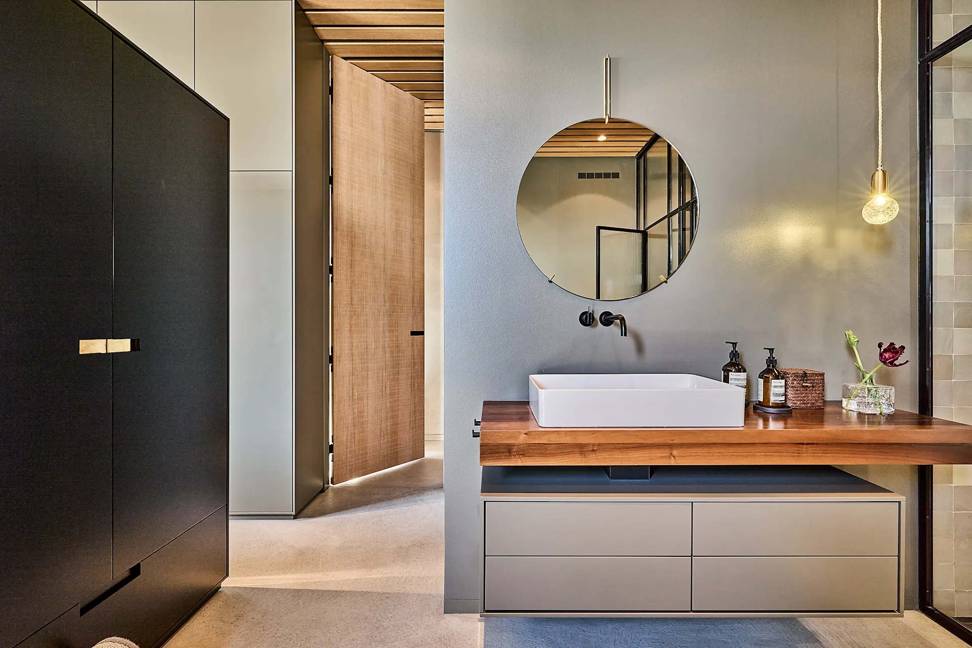 Modernes Badezimmer mit rechteckigem Waschbecken, rundem Spiegel und Holzwaschtisch.