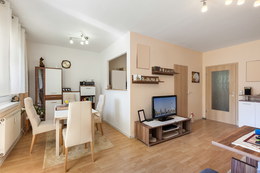Helles Wohnzimmer mit Essbereich, Holzboden, Esstisch und Fernseher auf kleinem Sideboard.