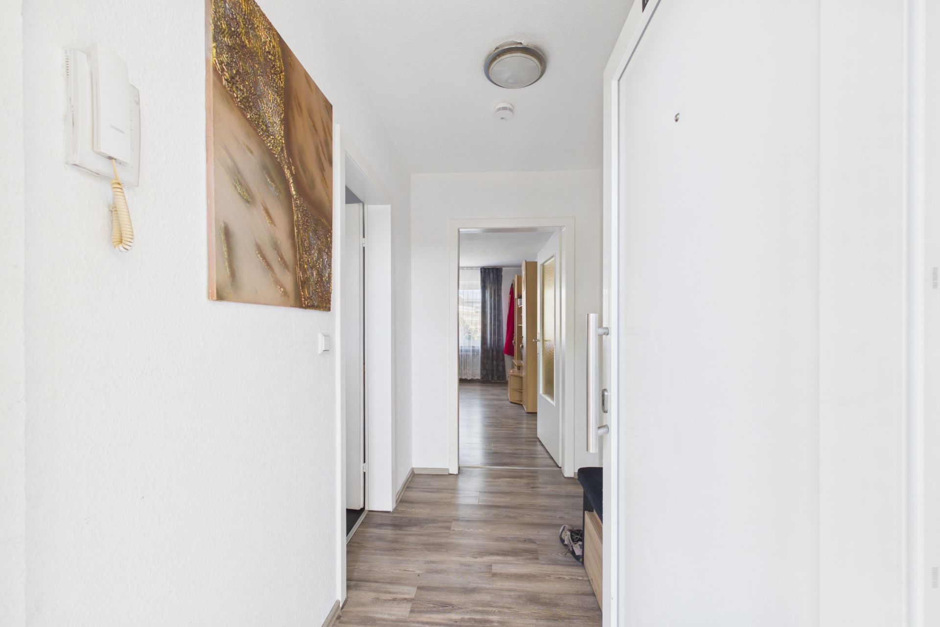 Heller Flur mit Holzfußboden, weißer Wand, Bild und Blick in weitere Zimmer.