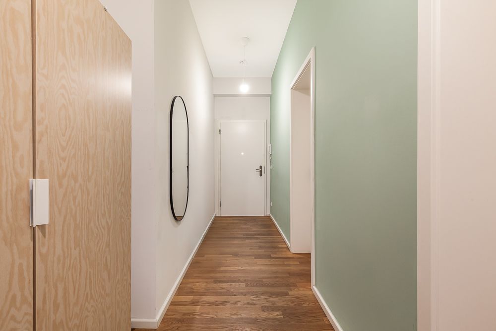 Heller Flur mit Holzboden, Spiegel an der Wand und einem Holzschrank links.