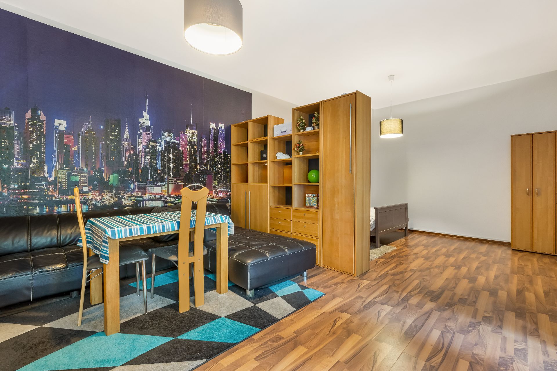 Wohnraum mit Holzboden, Regalwand, Sofa, Esstisch und großem Wandbild einer Skyline.