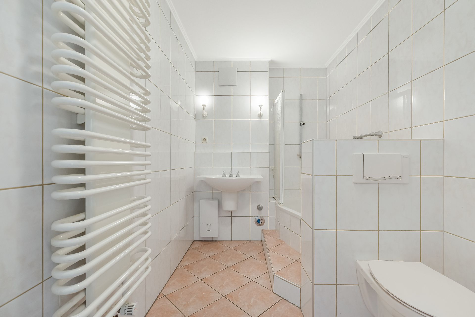 Helles Badezimmer mit weiß gefliesten Wänden, Waschbecken, Dusche, Handtuchheizkörper und Toilette.