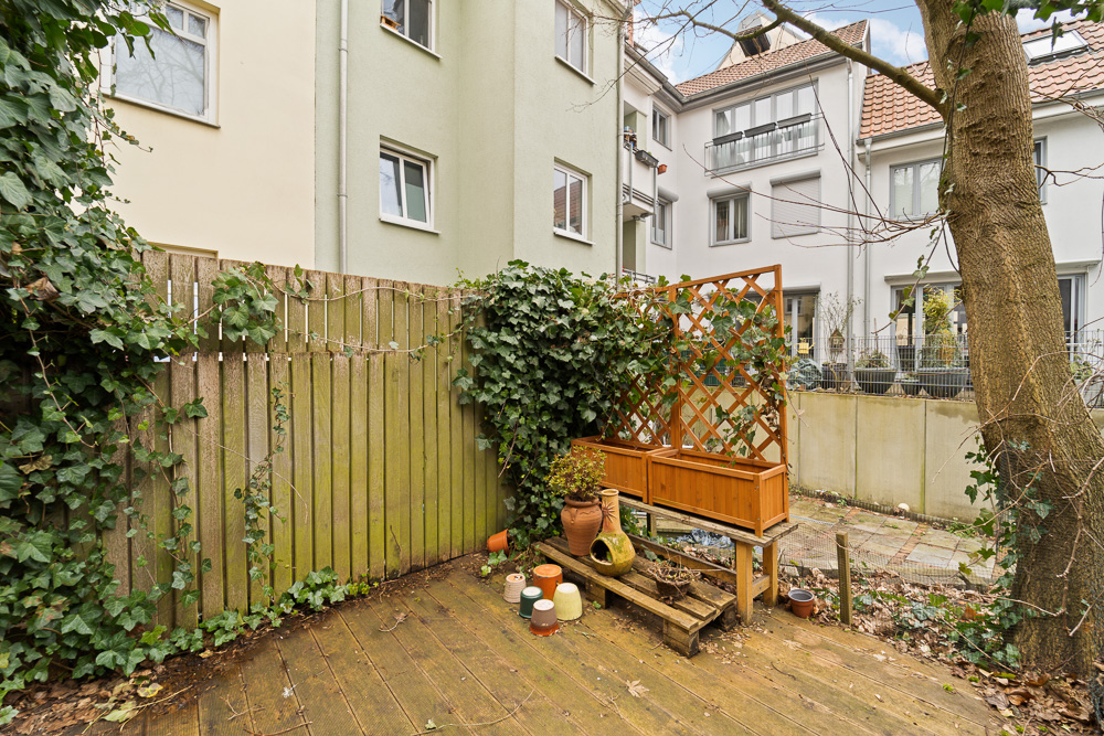 Kleiner Garten mit Holzzaun, Rankgitter, Blumentöpfen und angrenzendem Wohnhaus.