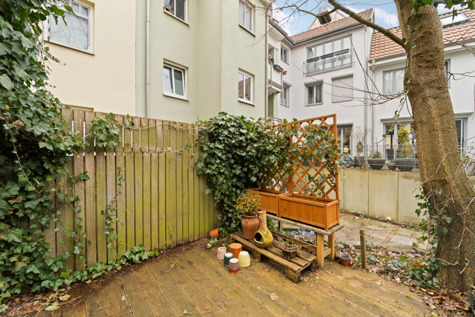 Kleiner Garten mit Holzzaun, Rankgitter, Blumentöpfen und angrenzendem Wohnhaus.