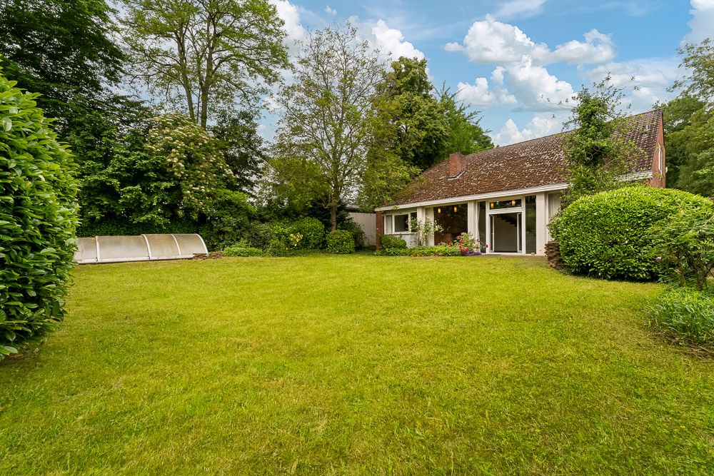 Großer Garten mit Rasenfläche, Büschen und Bäumen vor einem Haus mit Terrasse.