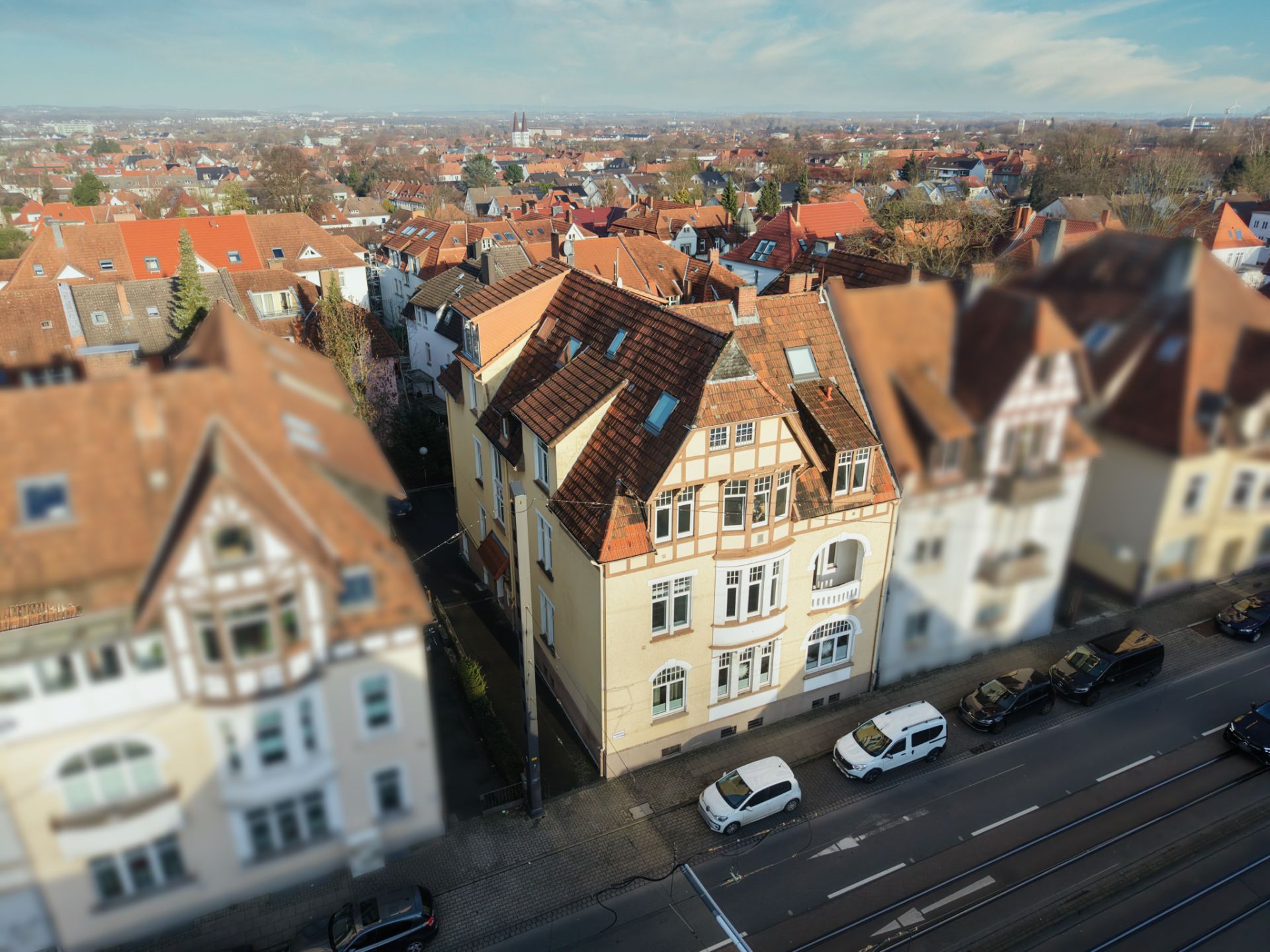 Mehrstöckiges Wohnhaus mit roten Dachziegeln an einer Straße, mehrere Autos davor geparkt.
