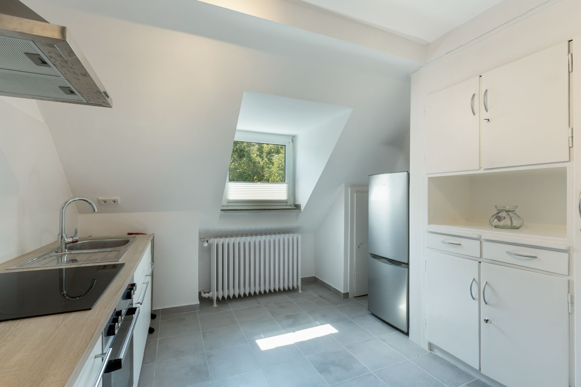 Helle Küche mit Fenster, Kühlschrank, Einbauschränken, Spüle und Herd.