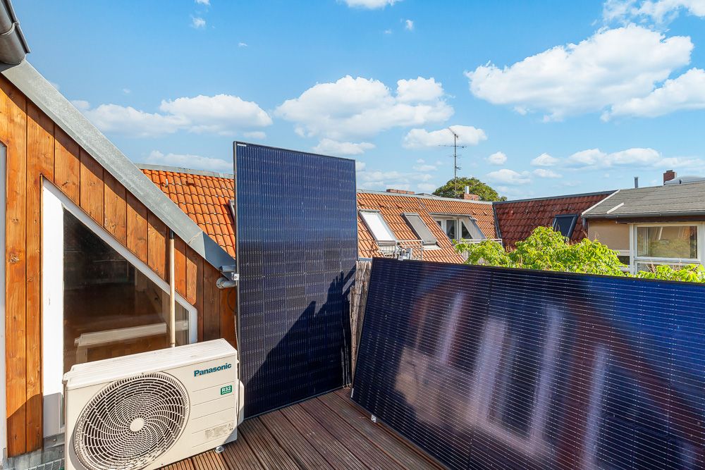 Holzverkleideter Balkon mit Solarpaneelen und Klimaanlage, Blick auf Nachbarhäuser.