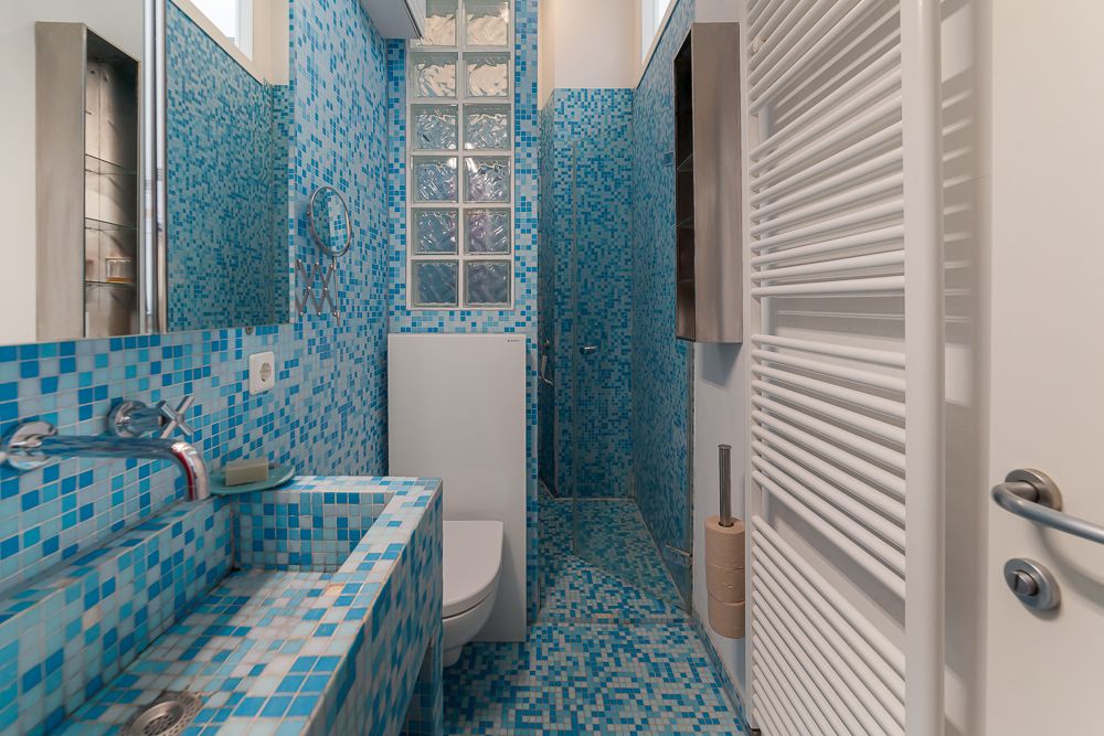 Modernes Badezimmer mit blauen Mosaikfliesen, Waschbecken, Toilette und Dusche.