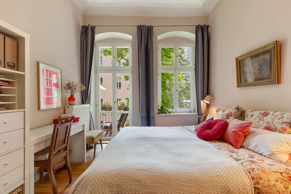 Helles Schlafzimmer mit Doppelbett, Schreibtisch, Stuhl und großen Fenstern mit Blick auf einen Balkon.