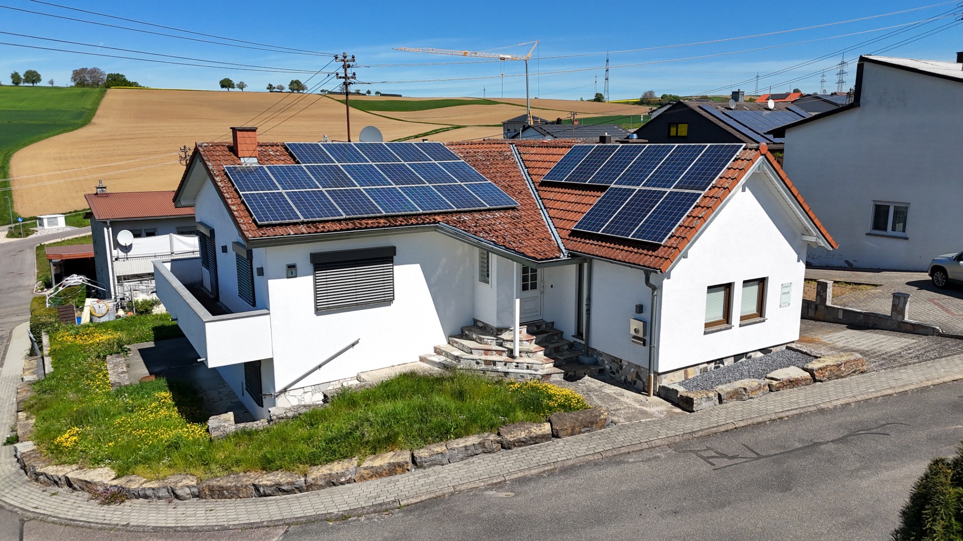 Weißes Einfamilienhaus mit Solarpanelen auf dem Dach und kleinem Garten vorne.