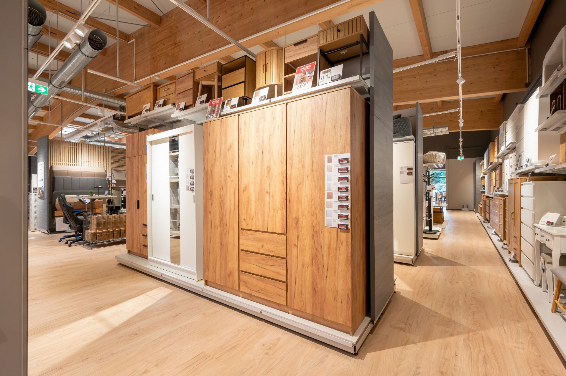 Großer Holzkleiderschrank mit Schubladen steht in einem Raum mit Holzdecke und sichtbaren Lüftungsrohren.