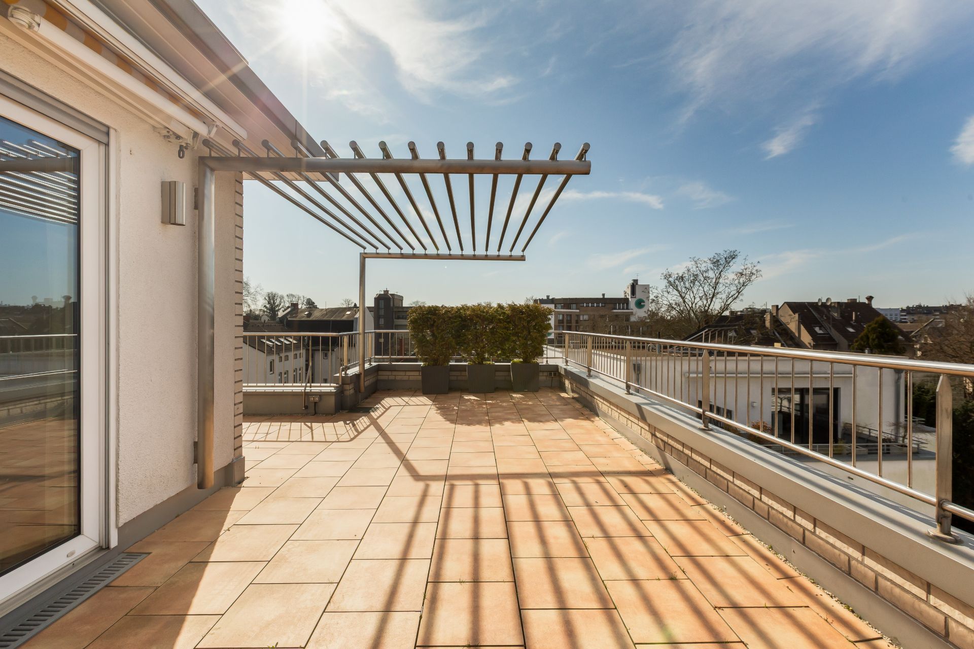 Große Dachterrasse mit Fliesenboden, Pergola und Pflanzkästen, umgeben von Geländer.