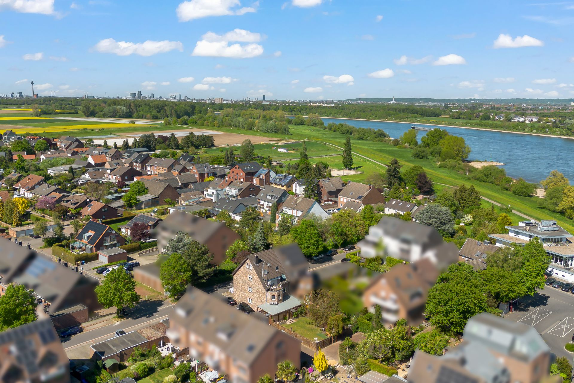 Luftbild einer Wohnsiedlung mit Häusern, Gärten und einem Fluss im Hintergrund.