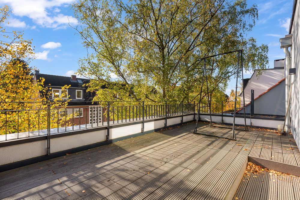 Große Dachterrasse mit Holzboden und Geländer, im Hintergrund Bäume und Nachbarhäuser.