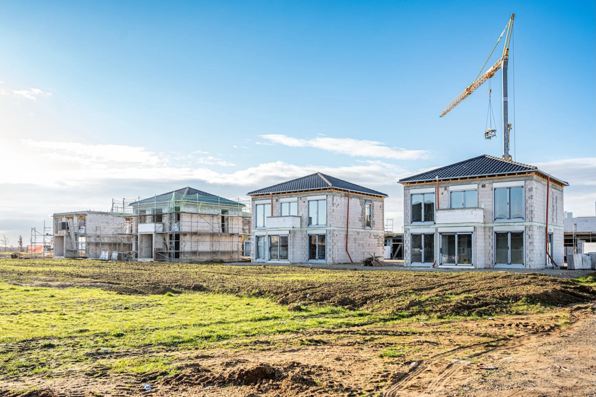 Mehrere Einfamilienhäuser im Rohbau mit Baukran und Gerüsten auf einer Baustelle.